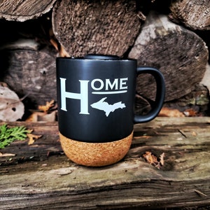 May include: Black ceramic mug with a cork bottom. The mug has a white graphic of the state of Michigan with the word "HOME" above it.