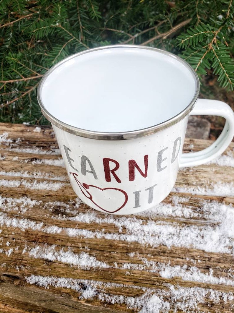 May include: White enamel camping mug with a silver rim. The mug has a red and silver design that says "Earned It".