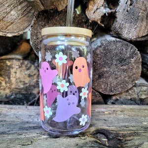 May include: A clear glass reusable water bottle with a bamboo lid and a straw. The bottle is decorated with pink, orange, and white ghost and flower designs.