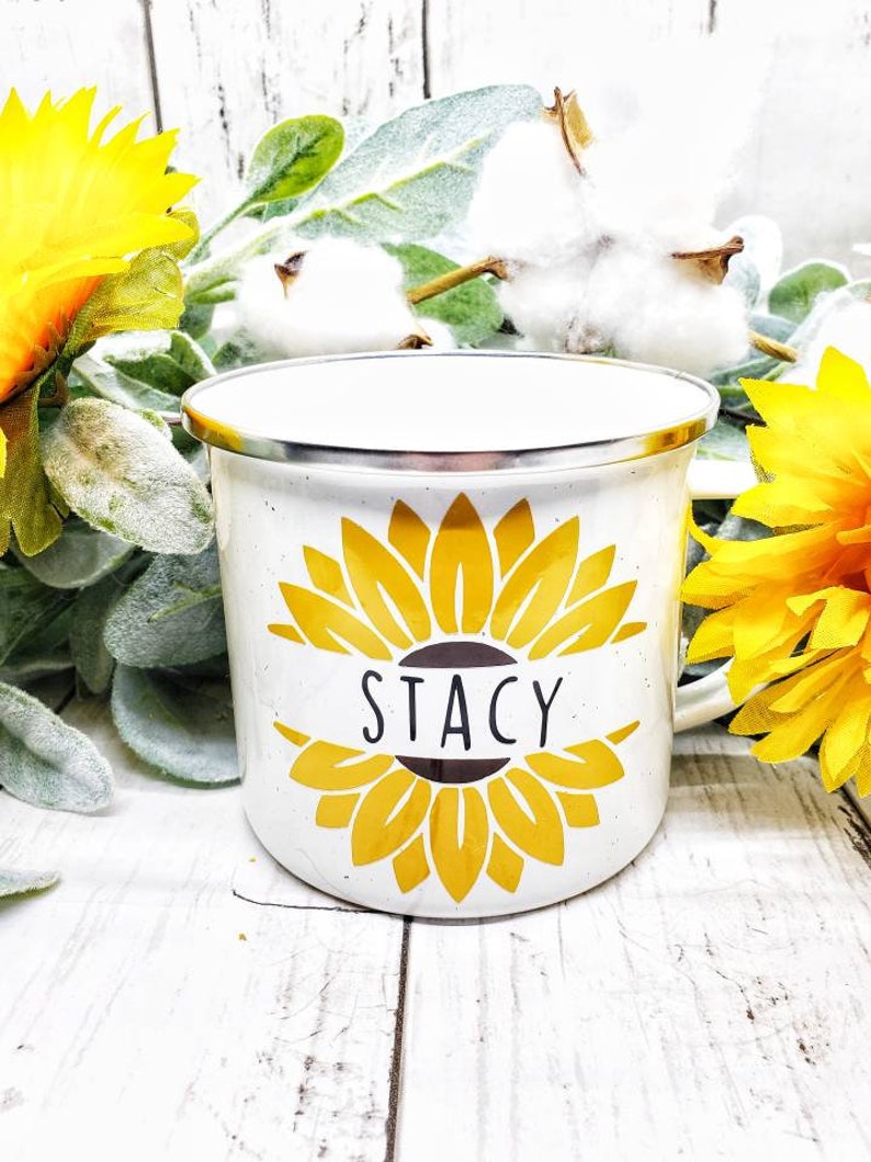 Op de afbeelding: Witte emaille mok met een geel zonnebloemontwerp en de naam "Stacy" in zwarte letters.