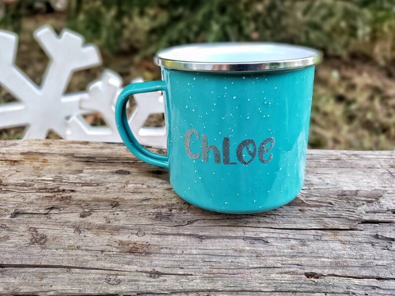 May include: A turquoise blue enamel camping mug with a silver rim and a white speckled finish. The mug has the name "Chloe" written in silver lettering.