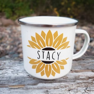 Op de afbeelding: Witte emaille mok met een geel zonnebloemontwerp en de naam "Stacy" in zwarte letters.