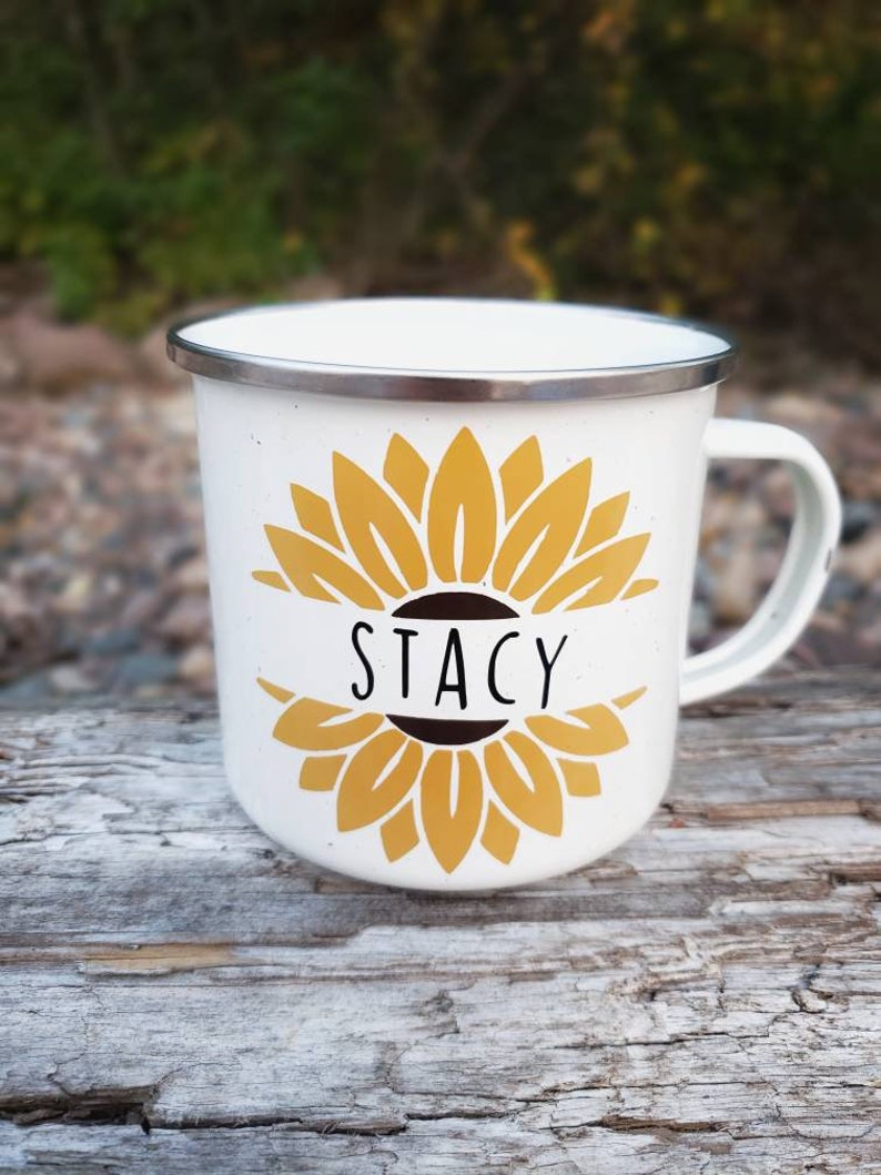 Op de afbeelding: Witte emaille mok met een geel zonnebloemontwerp en de naam "Stacy" in zwarte letters.