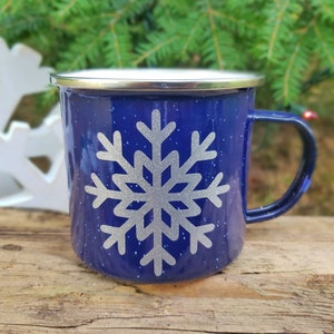 May include: A blue enamel mug with a silver snowflake design. The mug has a silver rim and a handle.
