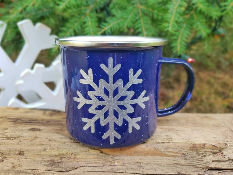 May include: A blue enamel mug with a silver snowflake design. The mug has a silver rim and a handle.