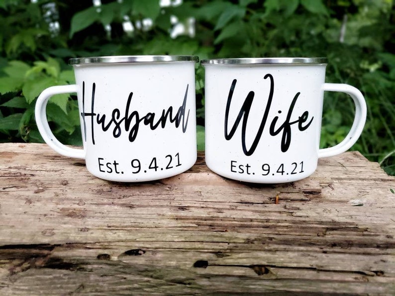 May include: Two white enamel mugs with black lettering. The mug on the left says "Husband Est. 9.4.21" and the mug on the right says "Wife Est. 9.4.21".