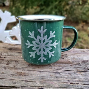 May include: A green enamel mug with a white snowflake design. The mug has a silver rim and handle.