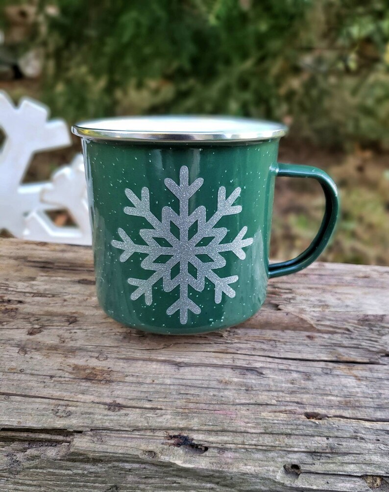 May include: A green enamel mug with a white snowflake design. The mug has a silver rim and handle.