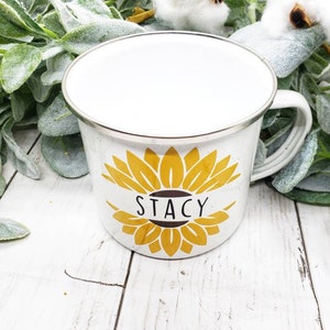 Op de afbeelding: Witte emaille mok met een zilveren rand en een geel zonnebloemontwerp. De zonnebloem heeft een bruin centrum met de naam "Stacy" in zwart.