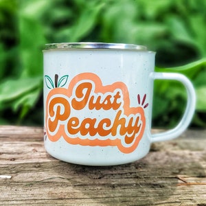 May include: White enamel mug with a peach design and the text "Just Peachy" in orange lettering.