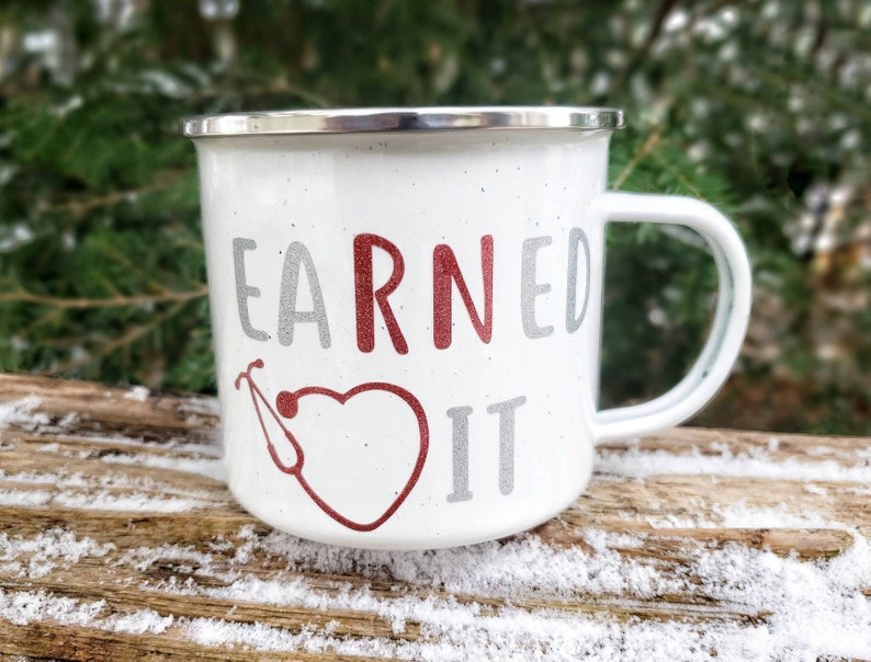 May include: White enamel mug with a red heart and a stethoscope design. The text "EARNED IT" is written in gray and red.