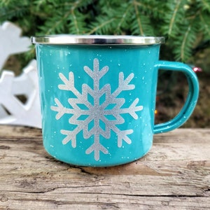 May include: A turquoise enamel mug with a silver snowflake design. The mug has a white speckled finish.