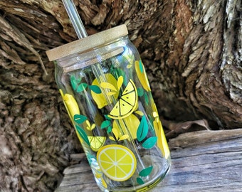 May include: A clear glass reusable water bottle with a bamboo lid and a glass straw. The bottle has a lemon print design with yellow lemons and green leaves.
