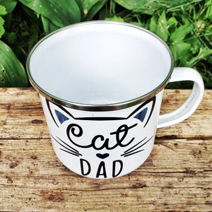 May include: White enamel mug with a black cat face and the text "Cat Dad" in black lettering.