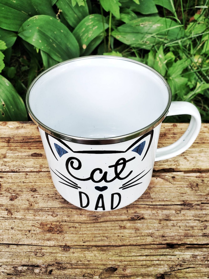 May include: White enamel mug with a black cat face and the text "Cat Dad" in black lettering.