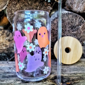 May include: A clear glass reusable can with a pink, orange, and purple ghost design and white flowers. The can has a clear plastic straw.