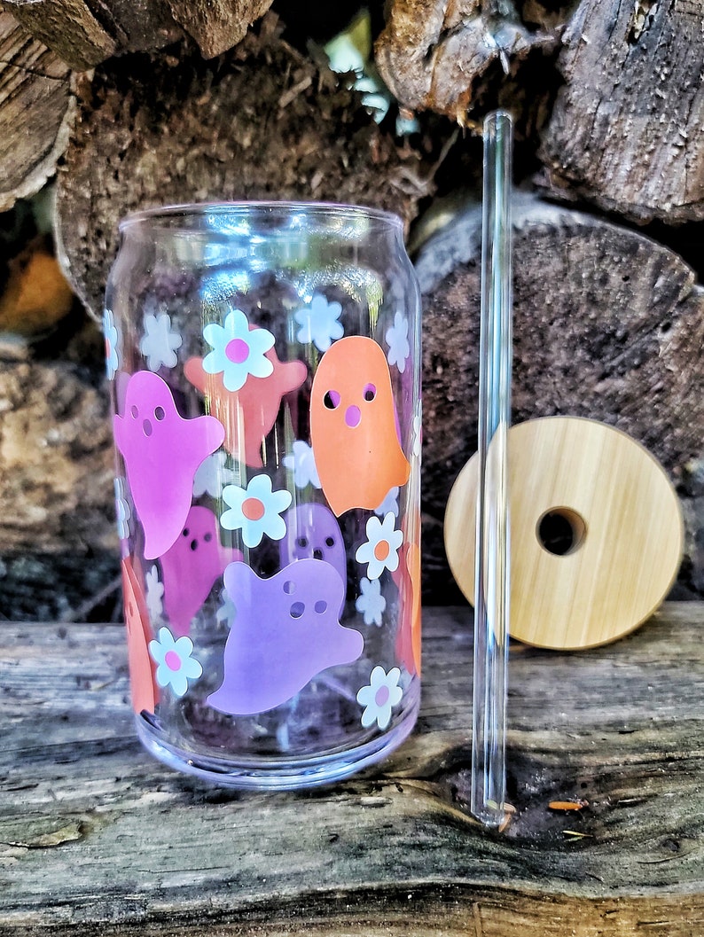 May include: A clear glass reusable can with a pink, orange, and purple ghost design and white flowers. The can has a clear plastic straw.