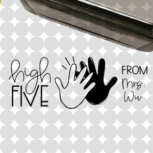 May include: Two black ink stamps with white text. The top stamp says "mrs. wu Likes this!" and the bottom stamp says "high FIVE" with two hands giving a high five. The text "FROM mrs. wu" is below the hands. A small blue circle with white text says "A Small World Called kindergarten" with a yellow pineapple graphic.