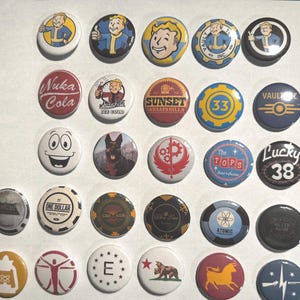May include: A collection of round pinback buttons with various designs and text. Some buttons feature cartoon characters, logos, and text such as "Nuka Cola", "Sunset Sarsaparilla", and "Lucky 38". The buttons are in various colors including yellow, blue, red, and black.