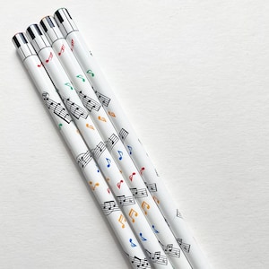 May include: Set of five white pencils with black musical notes and colorful treble clefs printed on them.