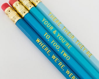 Könnte beinhalten: Satz mit vier blauen Ombre-Bleistiften mit goldener Beschriftung. Die Bleistifte sind beschriftet mit "THERE, THEIR, THEY'RE", "YOUR & YOU'RE", "TO, TOO, TWO" und "WHERE, WE'RE, WERE".