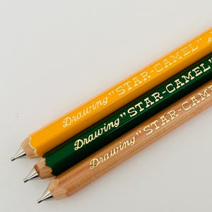 May include: Three pencils with yellow, green, and natural wood finishes. Each pencil has gold lettering that reads "Drawing "STAR-CAMEL"".