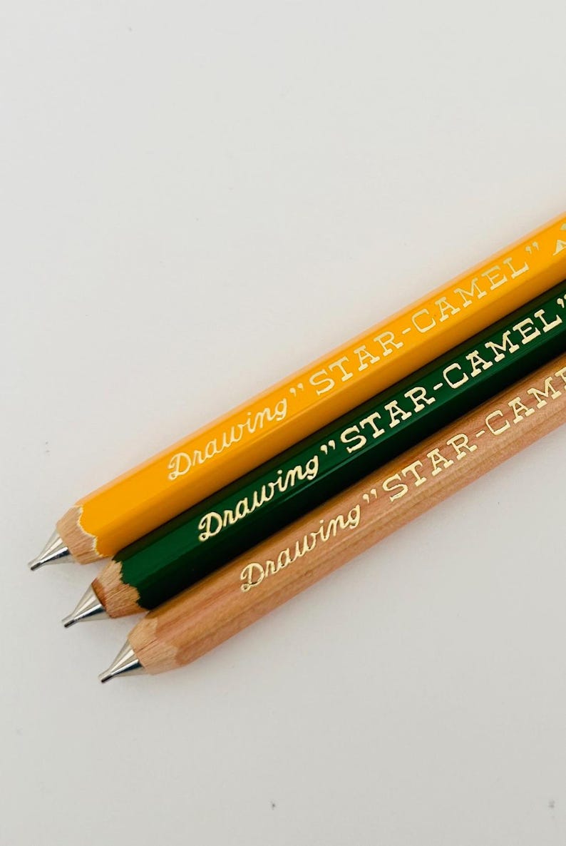 May include: Three pencils with yellow, green, and natural wood finishes. Each pencil has gold lettering that reads "Drawing "STAR-CAMEL"".