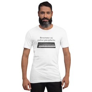以下が含まれることがあります： 白いTシャツに「Beware of false prophets」というテキストと、黒とグレーのシンセサイザーキーボードのグラフィックがプリントされています。