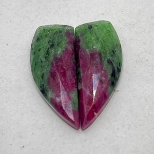Może przedstawiać: Dwa kamienie szlachetne w kształcie serca. Każdy kamień to mieszanka zielonych i czerwonych odcieni. Zielone obszary mają nakrapiany wygląd, podczas gdy czerwone sekcje są bardziej jednolite. Kamienie są cięte i polerowane, z gładką, odblaskową powierzchnią.
