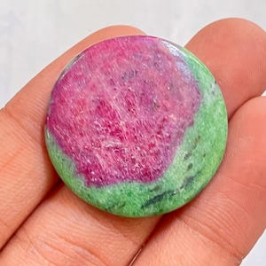 Op de afbeelding: Een ronde edelsteen met een levendige kleurencombinatie. Het midden heeft een rijke, dieproze tint, omringd door een ring van heldergroen. Het oppervlak van de steen heeft een licht getextureerd uiterlijk. Deze edelsteen is een unieke toevoeging aan elke collectie.