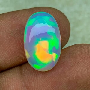 May include: An oval-shaped opal gemstone with a vibrant play of color. The stone displays a mix of green, blue, purple, and orange hues. The polished surface reflects light, showcasing the internal patterns and colors. This gemstone is suitable for jewelry making.