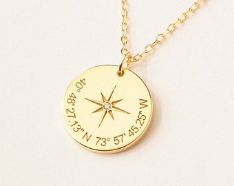 May include: A gold-toned necklace featuring a circular pendant with a central star compass design and a small embedded stone. The pendant is engraved with the coordinates 40° 48' 27.13" N 73° 57' 45.25" W and hangs from a delicate gold-toned chain.
