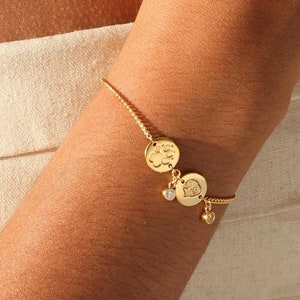 May include: A gold chain bracelet with three round charms. The charms feature a paw print, a heart, and a small diamond.