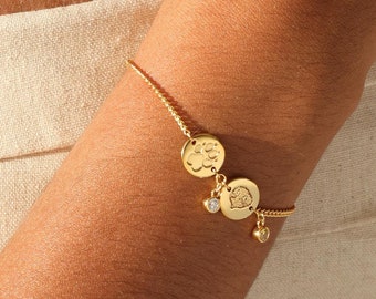May include: A gold chain bracelet with three round charms. The charms feature a paw print, a heart, and a small diamond.