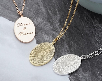 May include: Three oval pendant necklaces on delicate chains. One rose gold pendant is engraved with the text Oliver & Maria. One gold pendant and one silver pendant each feature a detailed, textured fingerprint design on the front surface.