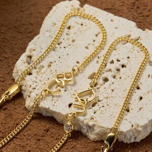 May include: Two gold chain bracelets with a small diamond accent. One bracelet has the word "Love" spelled out in cursive, and the other has the word "Best" spelled out in cursive.