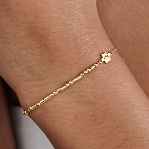 May include: A gold bracelet with a small paw print charm. The bracelet is made of tiny gold beads.