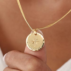 May include: A gold-colored necklace with a round pendant featuring a compass rose design. The pendant is suspended from a delicate chain. The necklace is a piece of jewelry.
