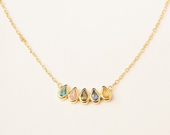 Può includere: Una collana con catena d'oro con una fila di cinque pietre preziose a forma di goccia in tonalità di blu, verde, rosa e giallo.