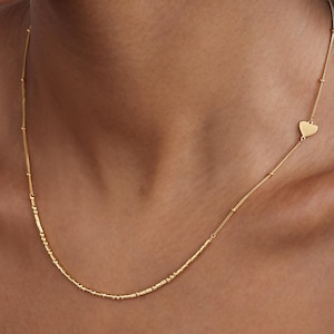 May include: A gold necklace with a delicate chain and small beads. A heart charm hangs from the chain.
