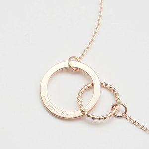 A rose gold infinity necklace with engraving Love you always, Mom engraved on the pendant. The infinity symbol is represented by two interlinked circles: one large and flat, and one small with a twist, giving it a standout and distinctive look.