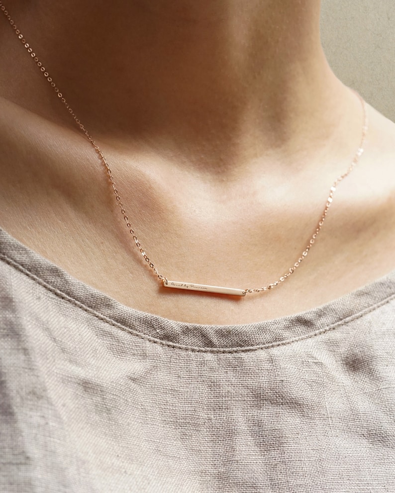 May include: A delicate gold chain necklace with a thin bar pendant that reads "loved by nature".