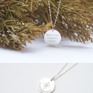 The photo has two faces of the circle necklace. The front side is engraved with a compass symbol at the center, then a coordinates underneath the compass symbol. The back side is engraved with My heart is a compass, it always leads me back to you