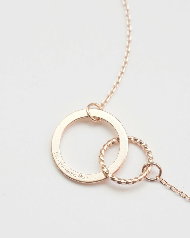 A rose gold infinity necklace with engraving Love you always, Mom engraved on the pendant. The infinity symbol is represented by two interlinked circles: one large and flat, and one small with a twist, giving it a standout and distinctive look.