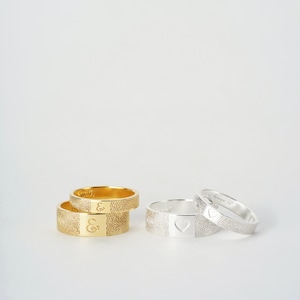 A couple gold ring and silver ring are standing on a white background. One ring for men, which is 7mm wide, and one ring for woman, which is 4mm wide. The fingerprint engraves outside of the ring, and the inscription engraves inside of the ring.