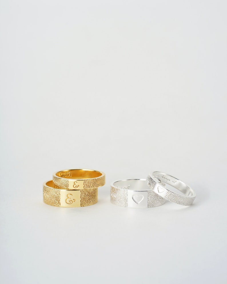 A couple gold ring and silver ring are standing on a white background. One ring for men, which is 7mm wide, and one ring for woman, which is 4mm wide. The fingerprint engraves outside of the ring, and the inscription engraves inside of the ring.