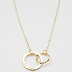 May include: A gold necklace with two interlocking circles. The larger circle has the coordinates "32.7489&deg; S, 152.1511&deg; E" engraved on it.