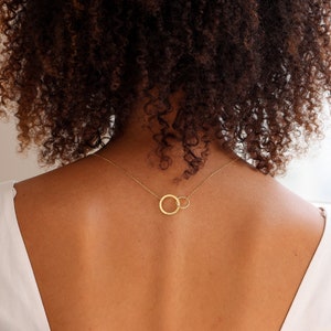 May include: A gold necklace with two interlocking circles. The necklace is worn by a person with curly brown hair.