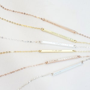 May include: A collection of personalized bar necklaces with different engravings. The necklaces are made of gold, silver, and rose gold chains with matching bar pendants. The engravings include names, dates, and Roman numerals.