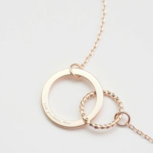 A rose gold infinity necklace with engraving Love you always, Mom engraved on the pendant. The infinity symbol is represented by two interlinked circles: one large and flat, and one small with a twist, giving it a standout and distinctive look.
